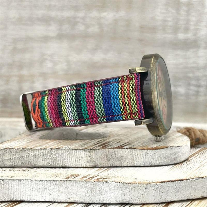 Bunte Armbanduhr mit gewebtem Textilarmband auf Holzuntergrund, handgefertigt, modisch, einzigartiges Design, nachhaltige Materialien.