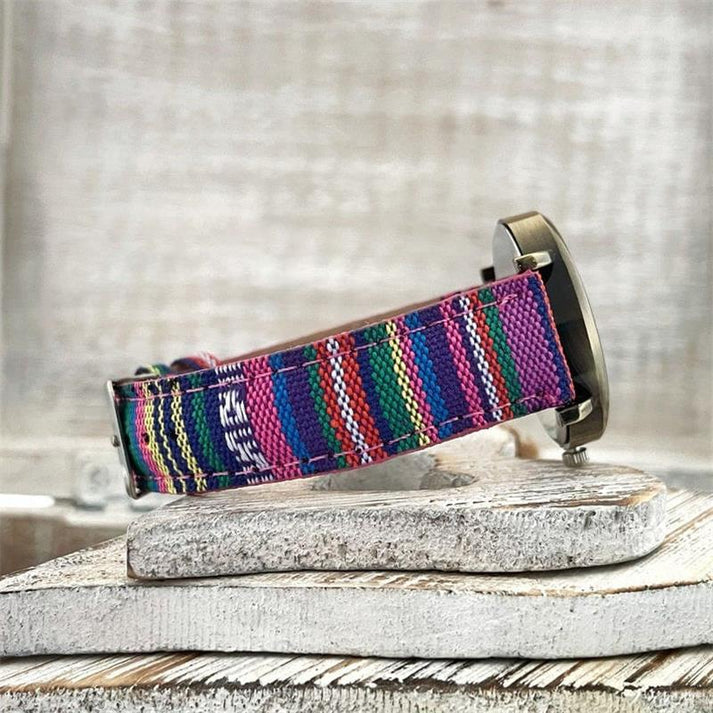 Bunte Armbanduhr mit gestreiftem Stoffarmband in Pink, Blau und Grün auf rustikalem Holzuntergrund. Modische Accessoires, trendige Uhren.