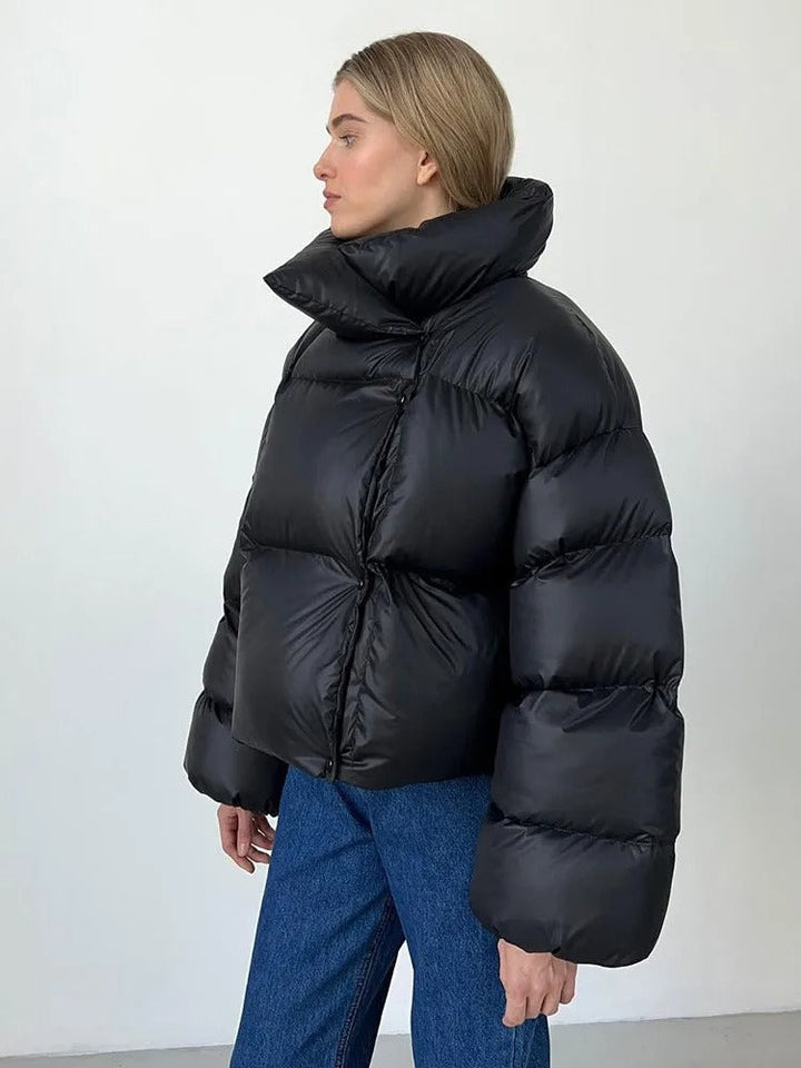 Frau in schwarzer Daunenjacke, seitlich, mit blonden Haaren, trägt blaue Jeans. Wintermode, warme Kleidung, modische Daunenjacke.