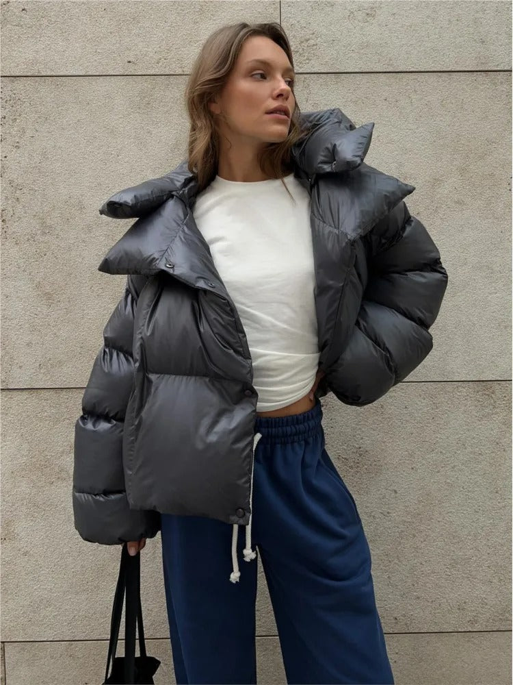 Frau in grauer Daunenjacke und blauer Jogginghose vor Betonwand. Modetrend, Winteroutfit, lässiger Stil, urbane Mode.