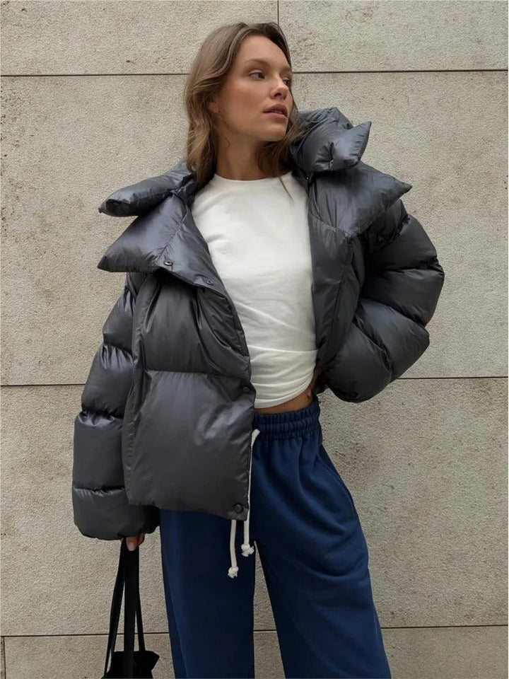 Frau in grauer Daunenjacke und blauer Jogginghose vor Betonwand. Modetrend, Winteroutfit, lässiger Stil, urbane Mode.