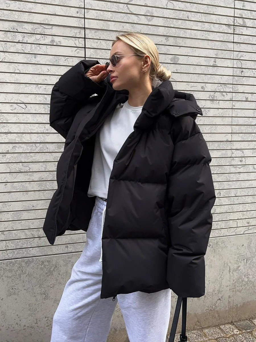 Frau in schwarzer Daunenjacke und weißem Sweatshirt vor gestreifter Wand. Wintermode, lässiger Stil, urbane Kleidung, modische Sonnenbrille.