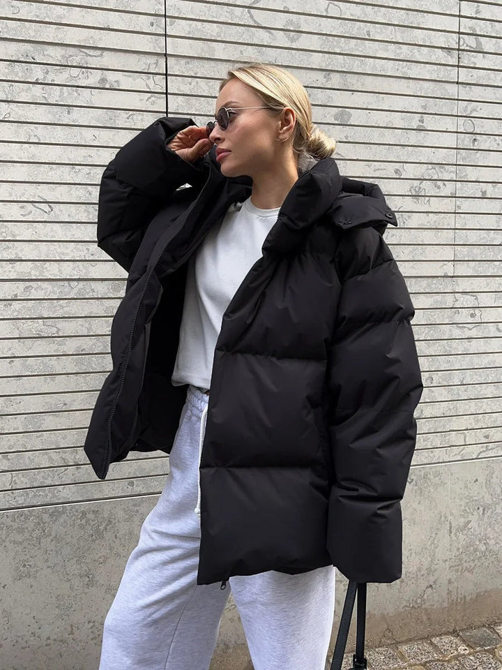 Frau in schwarzer Daunenjacke und weißem Sweatshirt vor gestreifter Wand. Wintermode, lässiger Stil, urbane Kleidung, modische Sonnenbrille.