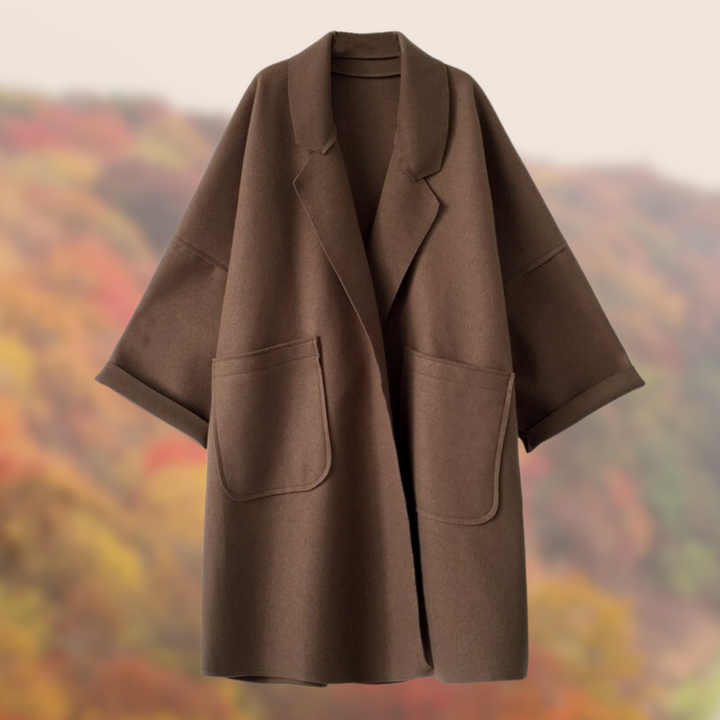 Brauner Wollmantel mit großen Taschen und weitem Schnitt vor herbstlichem Hintergrund. Eleganter Damenmantel, ideal für kühle Herbsttage.