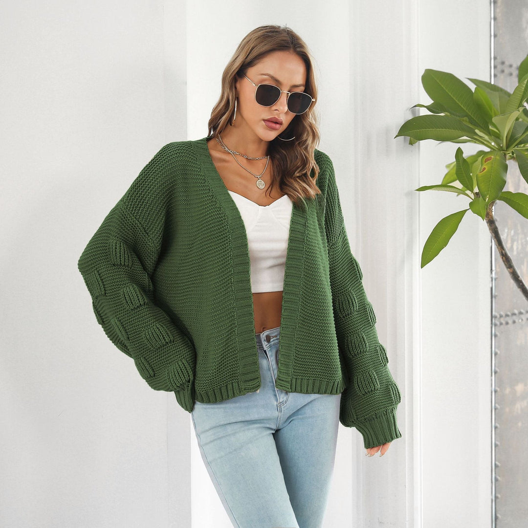 Frau in grünem Strickcardigan, weißem Top und blauer Jeans, trägt Sonnenbrille. Modetrend Herbst, lässiger Look, Damenmode.