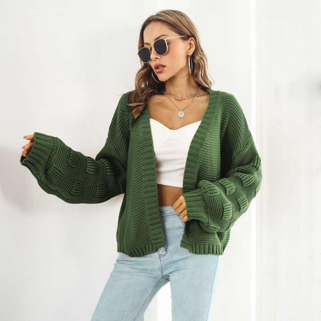 Frau in grünem Strickcardigan, weißem Top und blauer Jeans, trägt Sonnenbrille. Modetrend, lässiger Herbstlook, Damenmode.