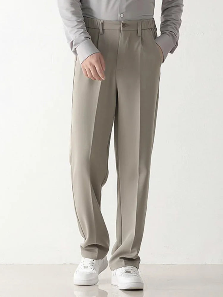 Graue Herren-Chinohose, locker geschnitten, mit seitlichen Taschen, kombiniert mit weißem Hemd und weißen Sneakers. Elegante Freizeitmode.