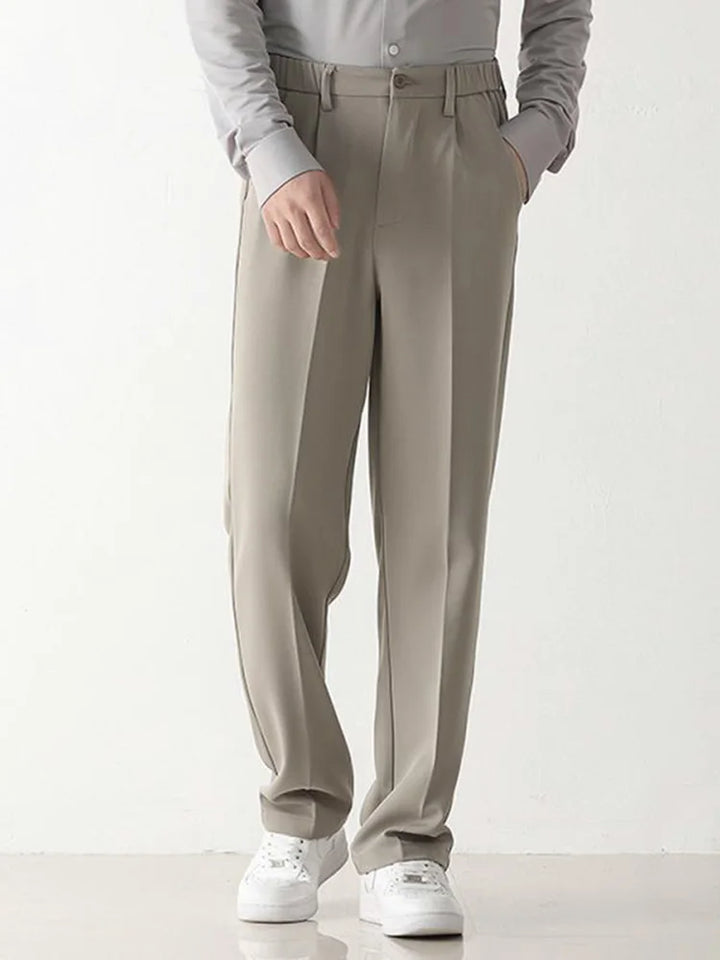Graue Herren-Chinohose, locker geschnitten, mit seitlichen Taschen, kombiniert mit weißem Hemd und weißen Sneakers. Elegante Freizeitmode.