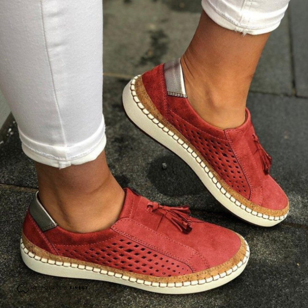 Rote Damen-Sneaker mit Fransen und perforiertem Design, getragen zu weißen Hosen. Bequeme Freizeitschuhe für den Alltag.
