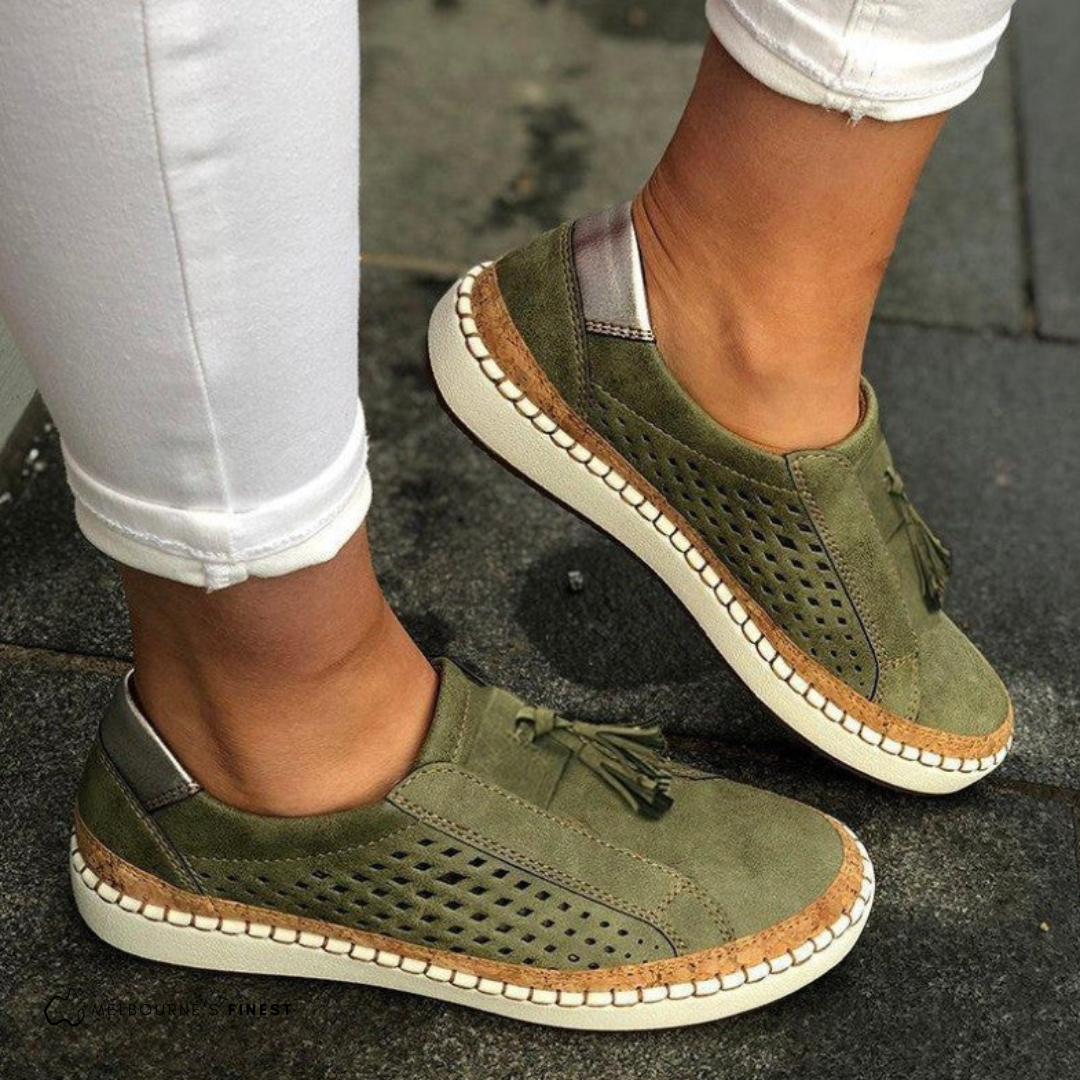 Grüne Damen-Sneaker mit Lochmuster und Fransen, kombiniert mit weißen Hosen. Bequeme Freizeitschuhe für den Alltag.