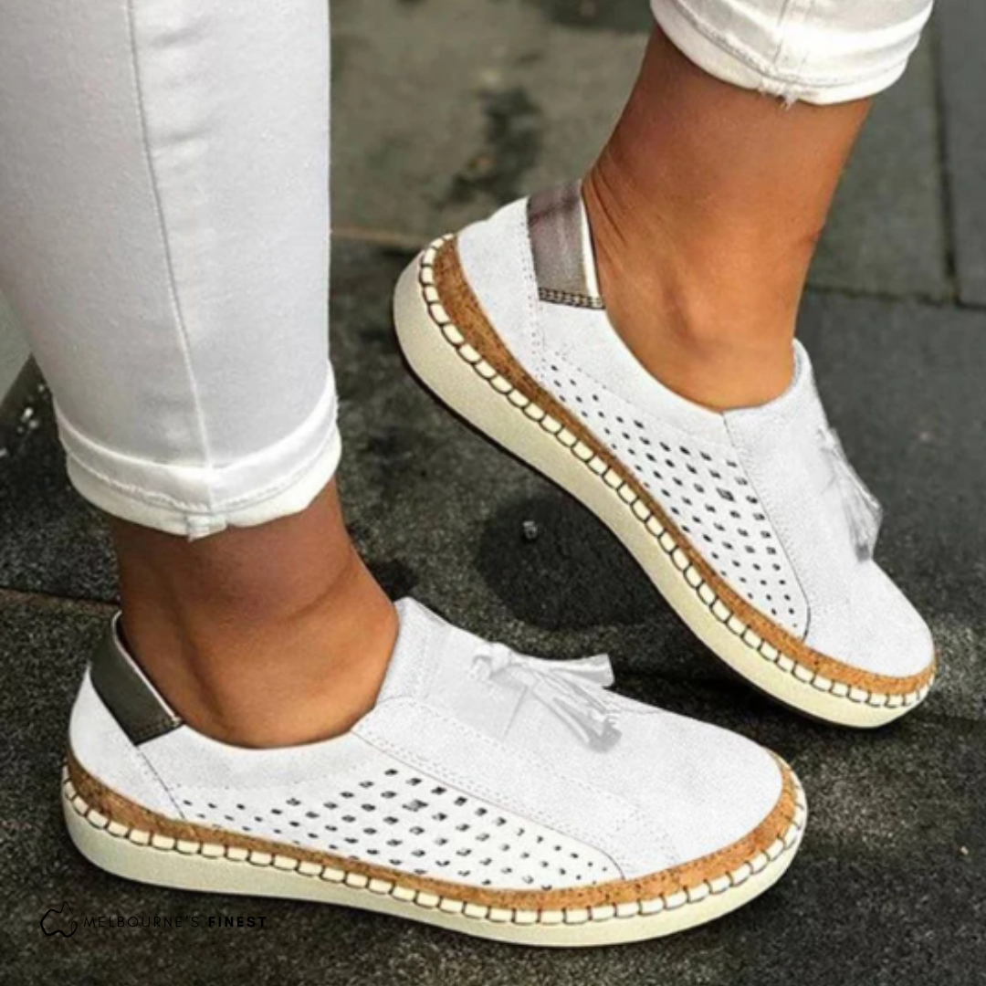 Weiße Damen-Sneaker mit Lochmuster und Bastsohle, getragen zu weißen Hosen. Modische, bequeme Sommerschuhe für Damen.