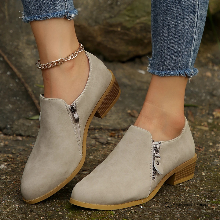 Damen-Slipper aus Wildleder in Beige mit seitlichem Reißverschluss, kombiniert mit blauen Jeans. Modische Schuhe für Herbst und Frühling.
