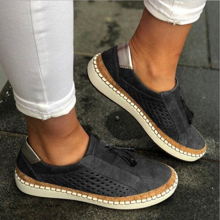 Damen Sneaker in Dunkelgrau mit Lochmuster und Quasten, kombiniert mit weißen Hosen. Bequeme Freizeitschuhe für den Alltag.