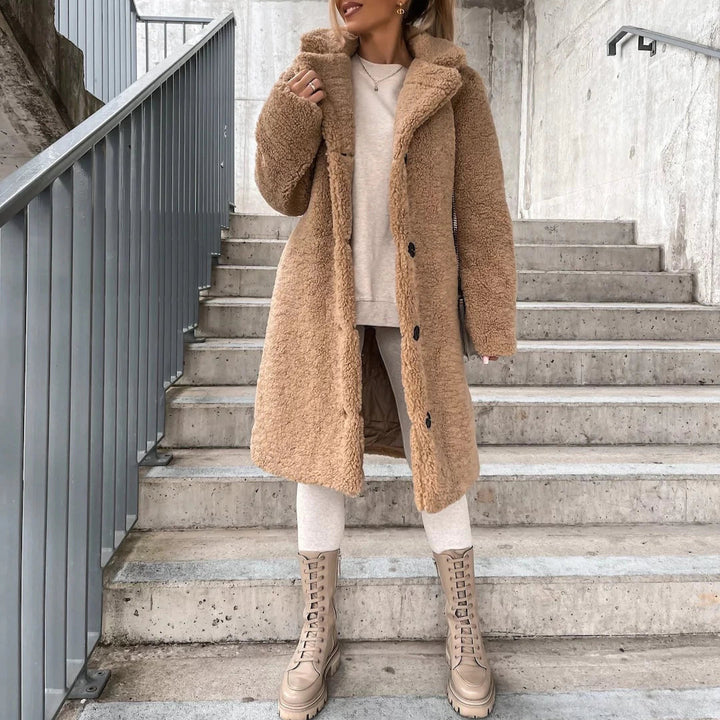 Frau in beigem Teddy-Mantel und Stiefeln auf Treppe, urbaner Hintergrund. Wintermode, Streetstyle, trendiger Look, warme Bekleidung.