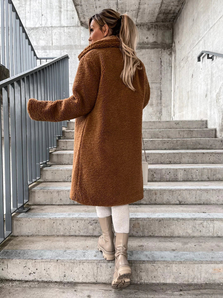 Frau in braunem Teddy-Mantel und beigen Stiefeln auf Treppe. Wintermode, Streetstyle, urbane Kleidung, trendiger Look.