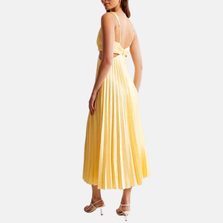 Frau in gelbem, plissiertem Sommerkleid mit Rückenausschnitt und Spaghettiträgern, trägt weiße Sandalen. Elegantes Damenmode-Outfit.