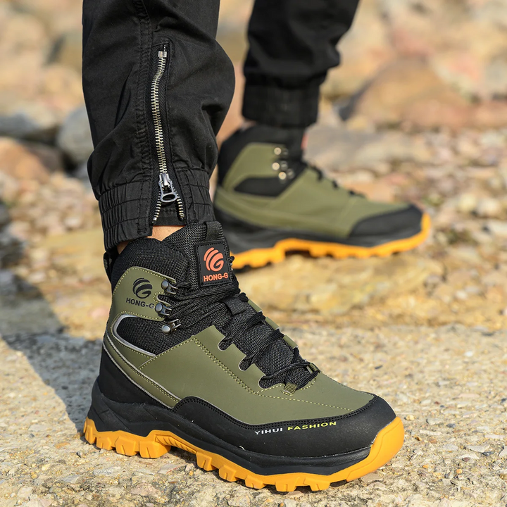 Hochwertige Outdoor-Wanderschuhe in Olivgrün und Schwarz mit gelber Sohle, getragen auf steinigem Untergrund. Ideal für Trekking und Abenteuer.