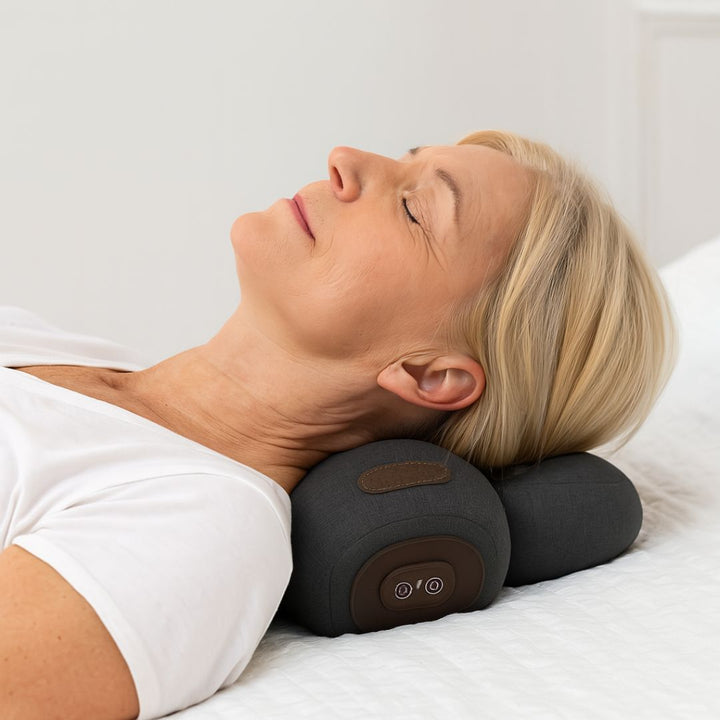 Frau, die ein Nackenmassagekissen auf einem Bett mit einfarbigem Hintergrund benutzt