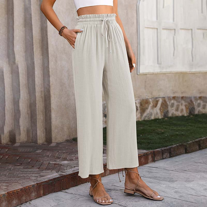 Frau trägt beige, weite Leinenhose mit Kordelzug, kombiniert mit Sandalen. Sommermode, lässiger Stil, bequeme Damenbekleidung.