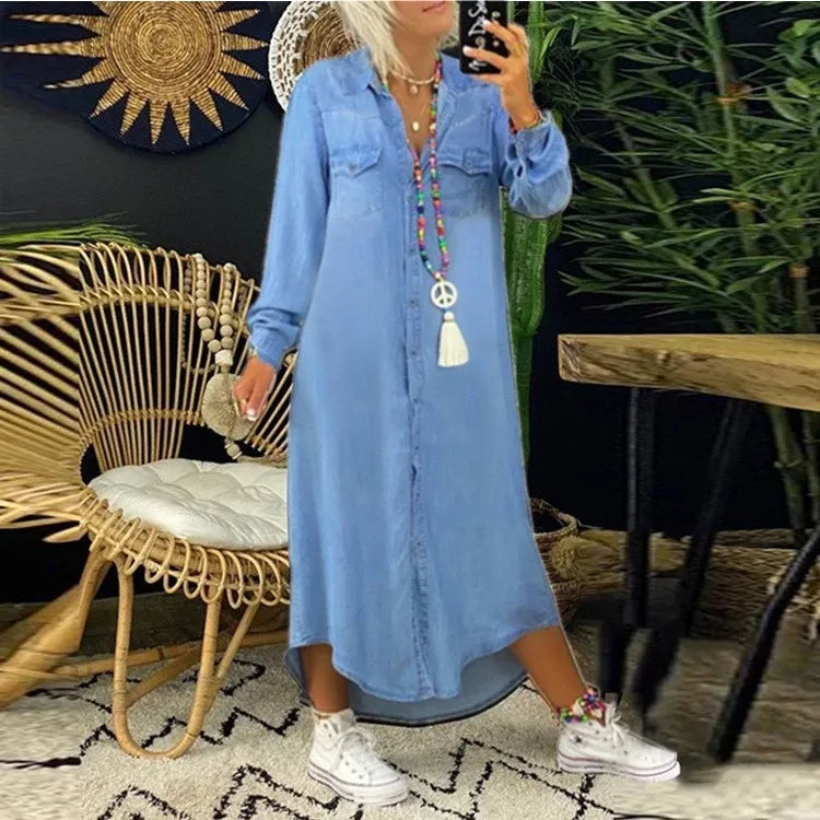 Frau in blauem Jeanskleid posiert vor Rattanmöbel, trägt weiße Sneakers und bunte Halskette. Boho-Dekor im Hintergrund.