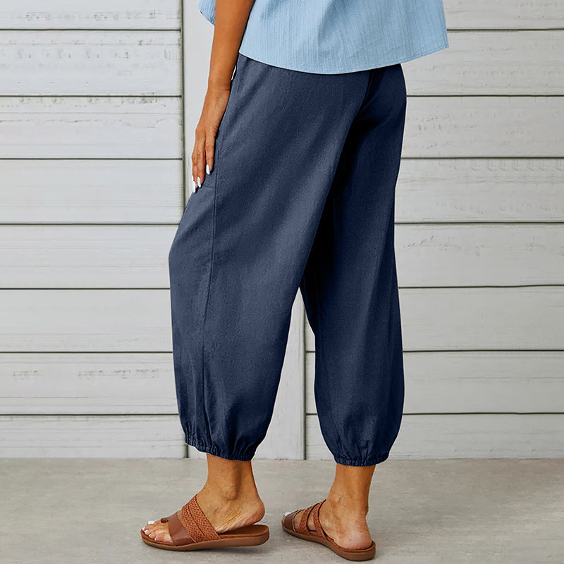 Frau trägt dunkelblaue Leinenhose mit elastischen Bündchen, kombiniert mit braunen Sandalen. Sommermode, bequeme Damenbekleidung, Freizeitlook.