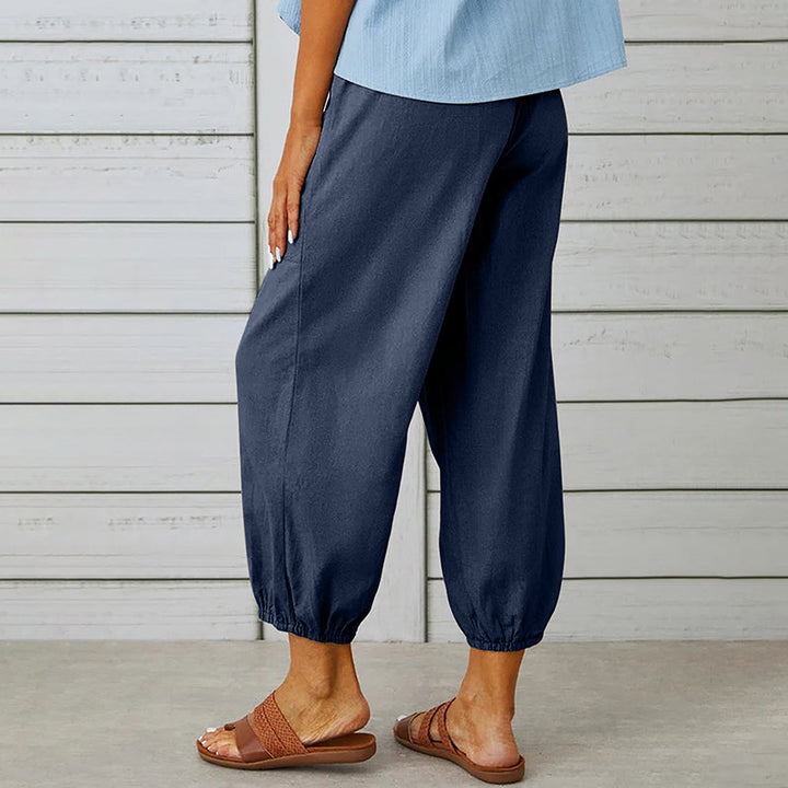 Frau trägt dunkelblaue Leinenhose mit elastischen Bündchen, kombiniert mit braunen Sandalen. Sommermode, bequeme Damenbekleidung, Freizeitlook.