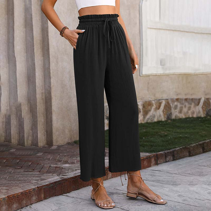 Dame in schwarzer, weiter Hose und Sandalen vor einer Steinmauer. Modetrend, Sommeroutfit, lässiger Stil, bequeme Damenbekleidung.