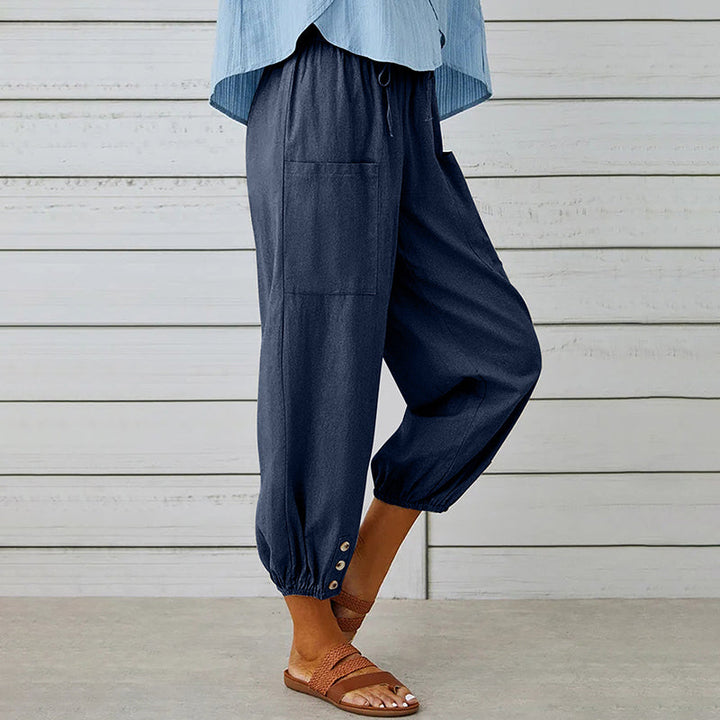 Frau trägt dunkelblaue Leinenhose mit Taschen und Knöpfen am Saum, kombiniert mit Sandalen. Perfekt für lässige Sommermode und Strandoutfits.