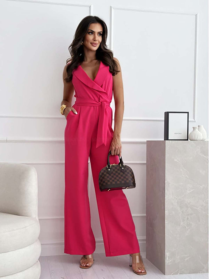 Frau in pinkem Jumpsuit posiert in modernem Wohnzimmer, hält eine Designer-Handtasche. Elegante Mode, stilvolle Damenbekleidung, trendiger Look.