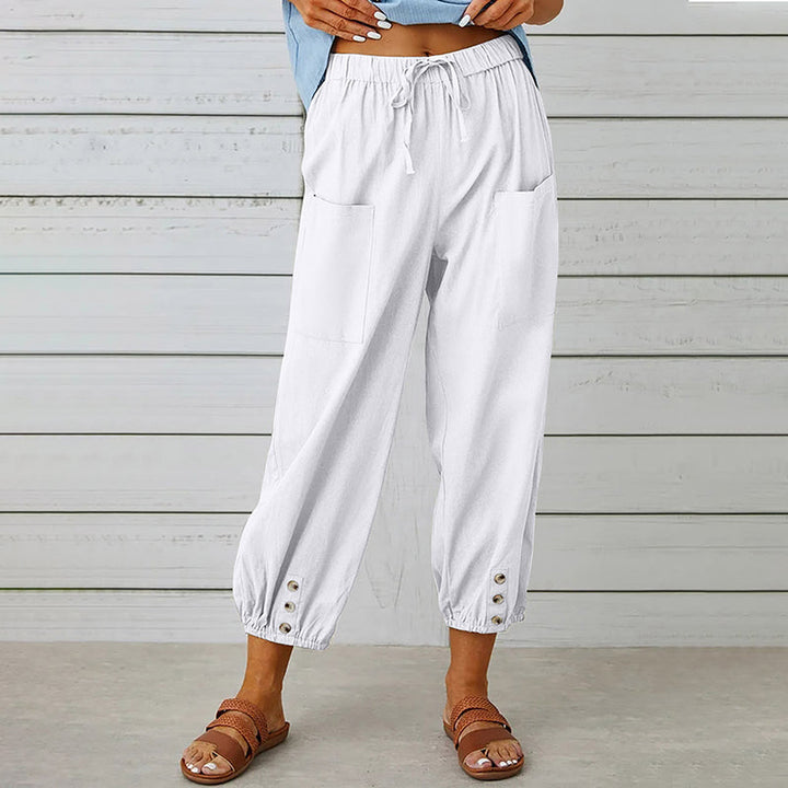 Frau trägt weiße Leinenhose mit Taschen und Knöpfen, kombiniert mit Sandalen. Sommermode, lässiger Stil, bequeme Damenbekleidung.