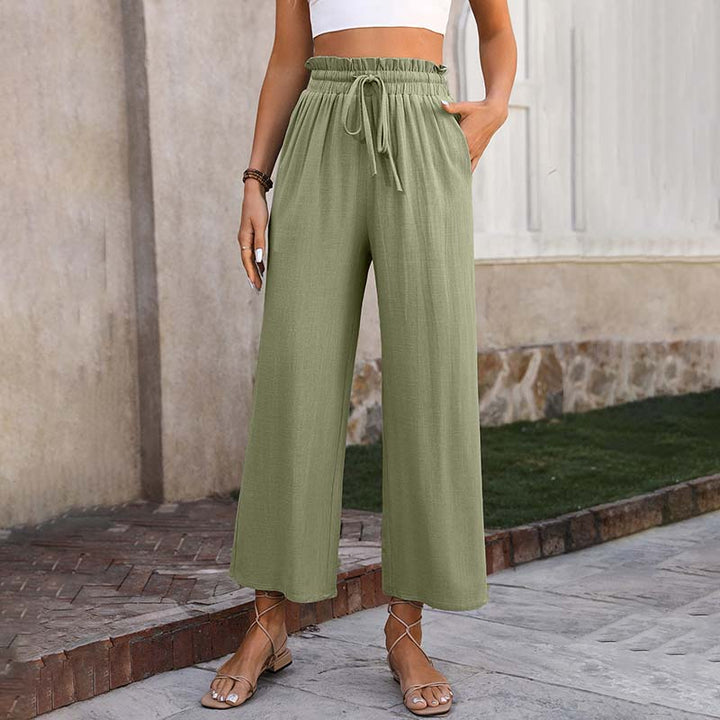 Frau in grüner Leinenhose und weißem Crop-Top, steht auf Gehweg. Sommermode, lässiger Stil, bequeme Kleidung, Sandalen.