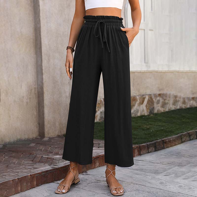 Frau trägt schwarze, weite Sommerhose mit Kordelzug, kombiniert mit Sandalen. Modetrend, lässiger Stil, bequeme Damenbekleidung.