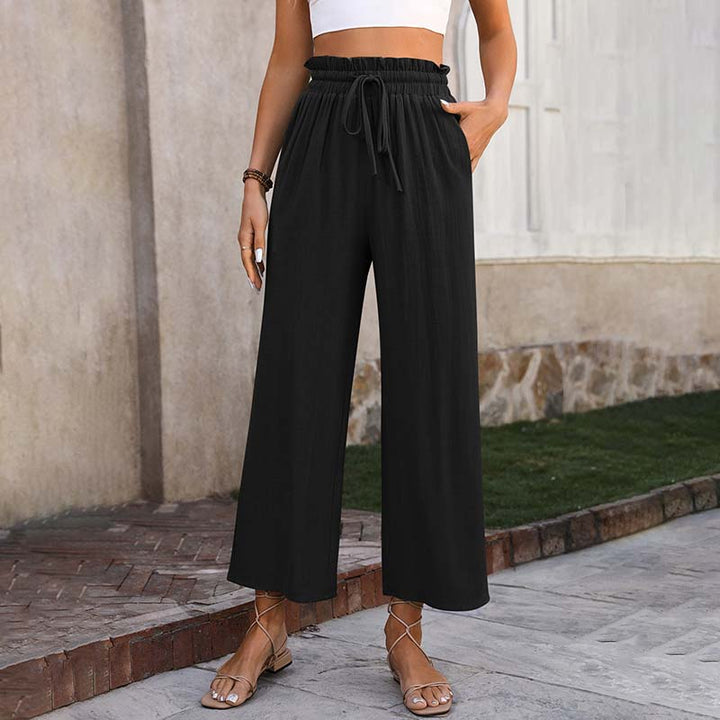 Frau trägt schwarze, weite Sommerhose mit Kordelzug, kombiniert mit Sandalen. Modetrend, lässiger Stil, bequeme Damenbekleidung.