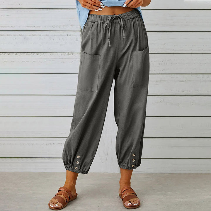 Frau trägt graue, lässige Haremshose mit Taschen und Knöpfen am Saum, kombiniert mit braunen Sandalen. Ideal für Sommermode und Freizeitkleidung.