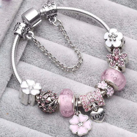 Silbernes Charm-Armband mit rosa Blumen- und Herzanhängern, verziert mit Kristallen, auf grauem Hintergrund. Elegantes Schmuckdesign für Damen.