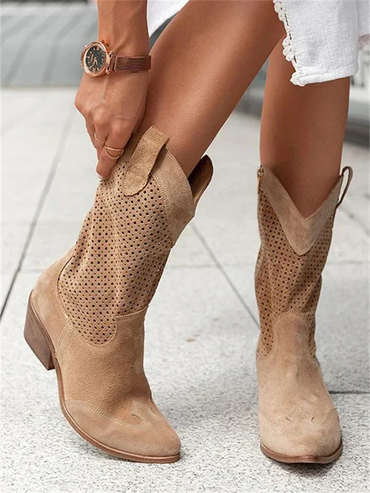 Damenbeine in beigen, perforierten Cowboystiefeln aus Wildleder auf Gehweg. Modische Stiefel, Sommerlook, trendige Damenmode.