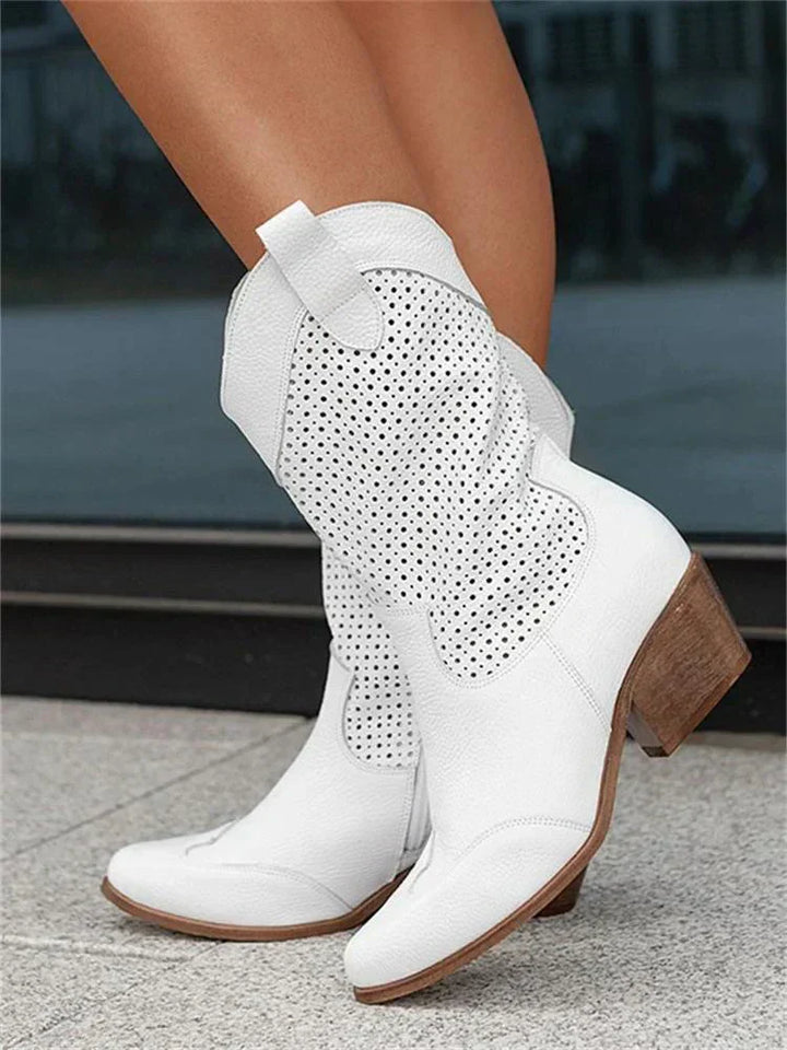 Weiße Cowboystiefel mit perforiertem Muster, niedriger Absatz, Damenmode, trendige Westernstiefel, stilvolle Schuhe auf grauem Boden.