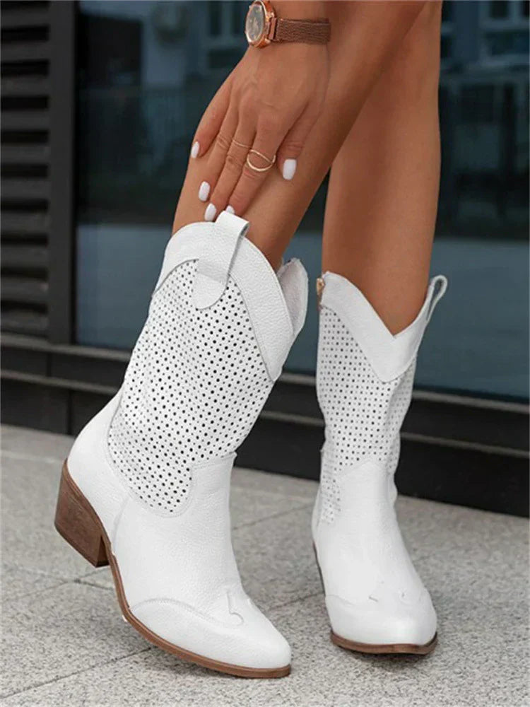 Weiße Cowboystiefel mit perforiertem Design, getragen von einer Person auf grauem Boden. Modische Damenstiefel, ideal für Sommer und Festivals.