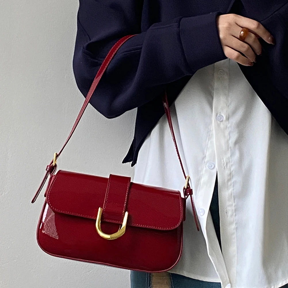 Damenhandtasche aus rotem Lackleder mit goldener Schnalle, getragen von Person in weißer Bluse und dunklem Blazer. Elegante Modeaccessoire.