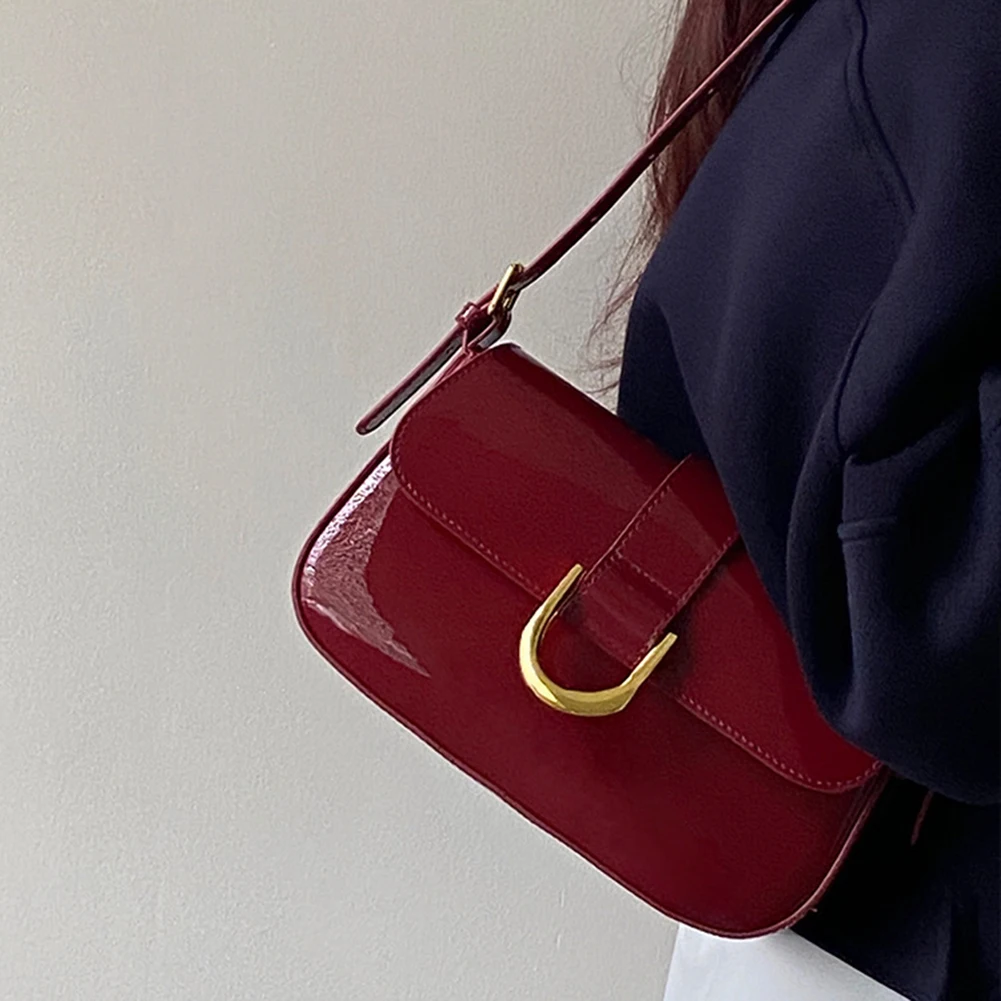 Dunkelrote Umhängetasche aus Leder mit goldener Schnalle, getragen von Person in schwarzem Oberteil. Elegante Damenhandtasche, modisches Accessoire.