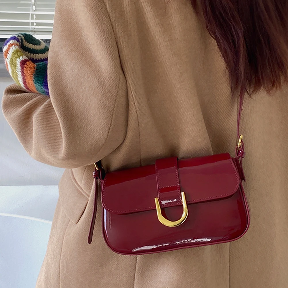 Damenhandtasche aus rotem Lackleder mit goldener Schnalle, getragen über einem beigen Mantel. Modische Umhängetasche, elegantes Accessoire.