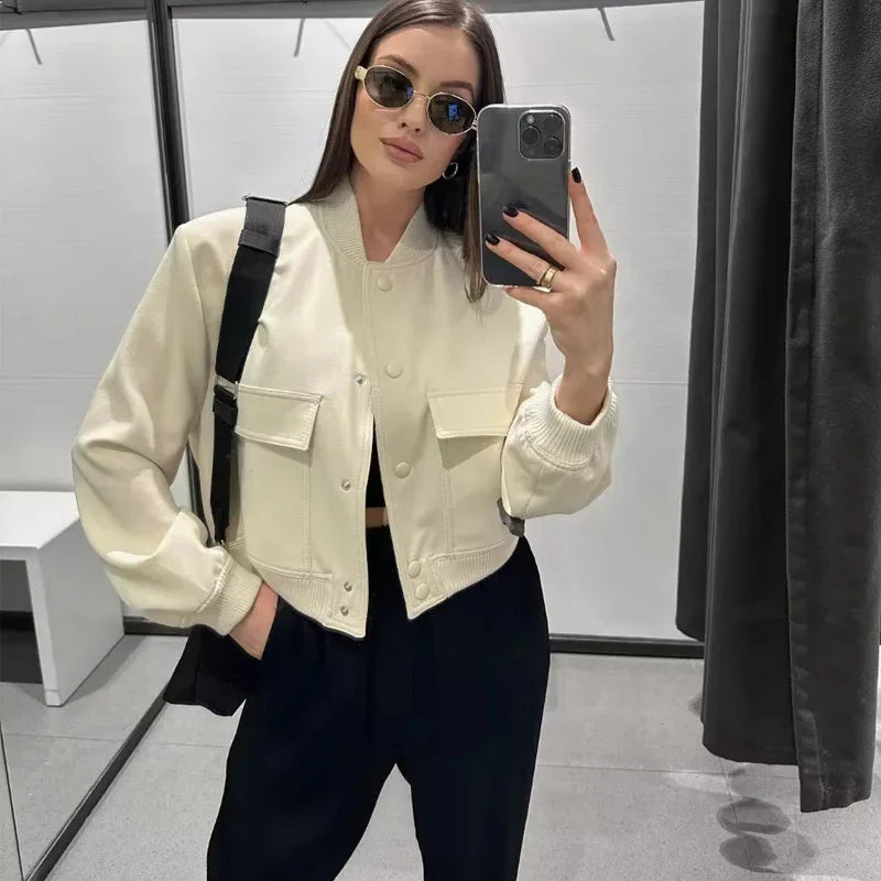 Frau im Umkleideraum, trägt weiße Jacke, schwarze Hose, Sonnenbrille, macht Selfie mit Smartphone. Modetrends, Damenmode, Streetstyle.