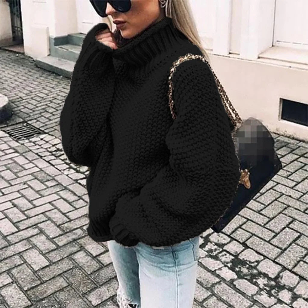 Frau in schwarzem Strickpullover und Sonnenbrille, trägt eine schwarze Handtasche, steht auf gepflasterter Straße. Modetrend, Herbstmode, Streetstyle.