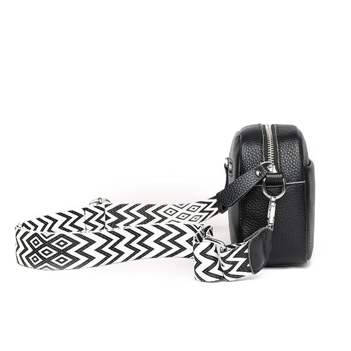 Schwarze Lederhandtasche mit geometrischem, schwarz-weißem Schultergurt, seitliche Ansicht. Modische Damenaccessoire, elegant und vielseitig.