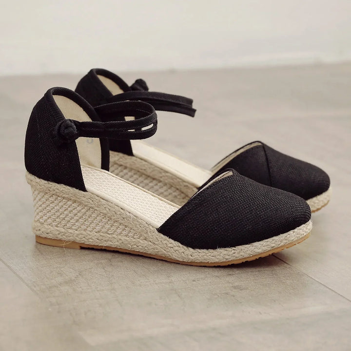 Schwarze Espadrilles mit Keilabsatz aus Jute auf Holzboden. Modische Sommerschuhe, ideal für Damen. Bequem und stilvoll für Freizeit und Alltag.