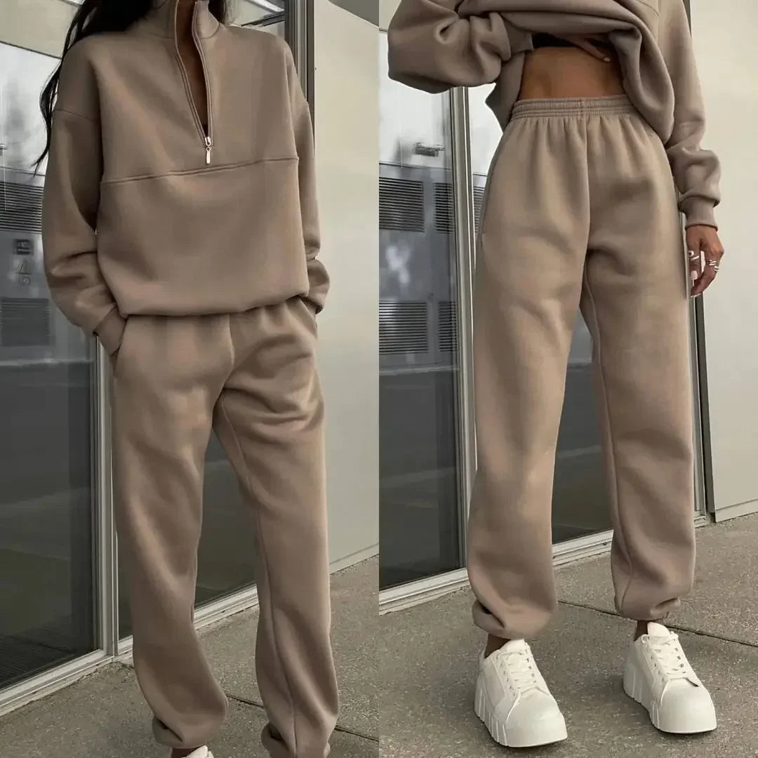 Frau in beigem Jogginganzug mit Reißverschluss und weißen Sneakern, moderne Freizeitmode, urbaner Hintergrund, stilvoll und bequem.