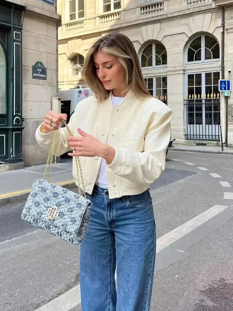 Junge Frau in weißer Jacke und blauer Jeans hält eine stilvolle Handtasche auf einer städtischen Straße. Mode, Streetstyle, Damenmode.