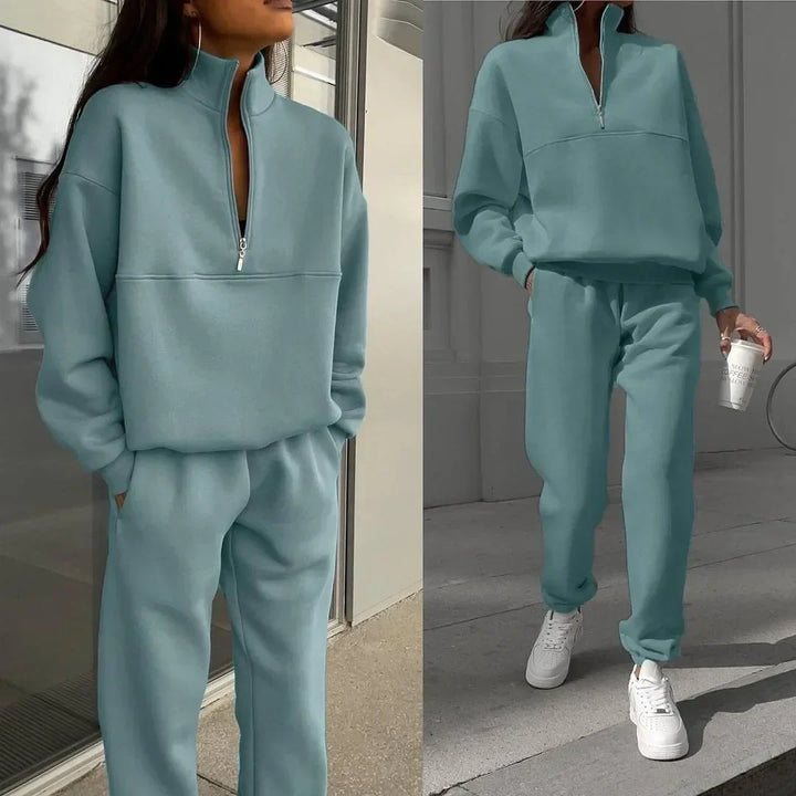Frau in hellblauem Jogginganzug mit Reißverschluss, lässig und modern, hält einen Kaffeebecher, trägt weiße Sneaker. Bequeme Freizeitmode.
