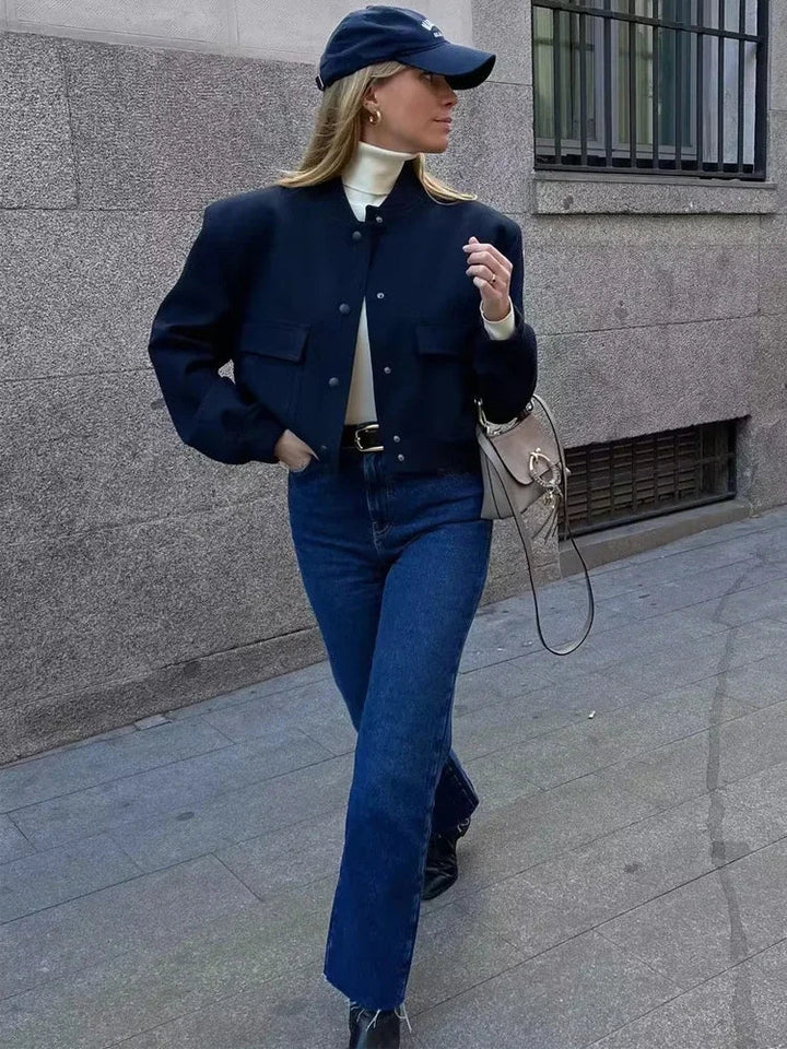 Frau in modischer Herbstkleidung: Dunkle Jacke, blaue Jeans, Baseballkappe und Umhängetasche. Streetstyle, lässig, urbaner Look.