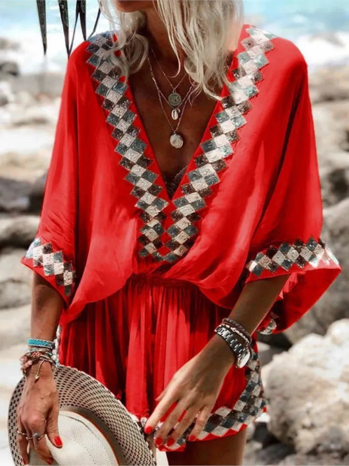 Frau in rotem Sommerkleid mit geometrischem Muster am Strand, hält Strohhut. Modetrend, Sommermode, Strandkleidung, Damenoutfit.